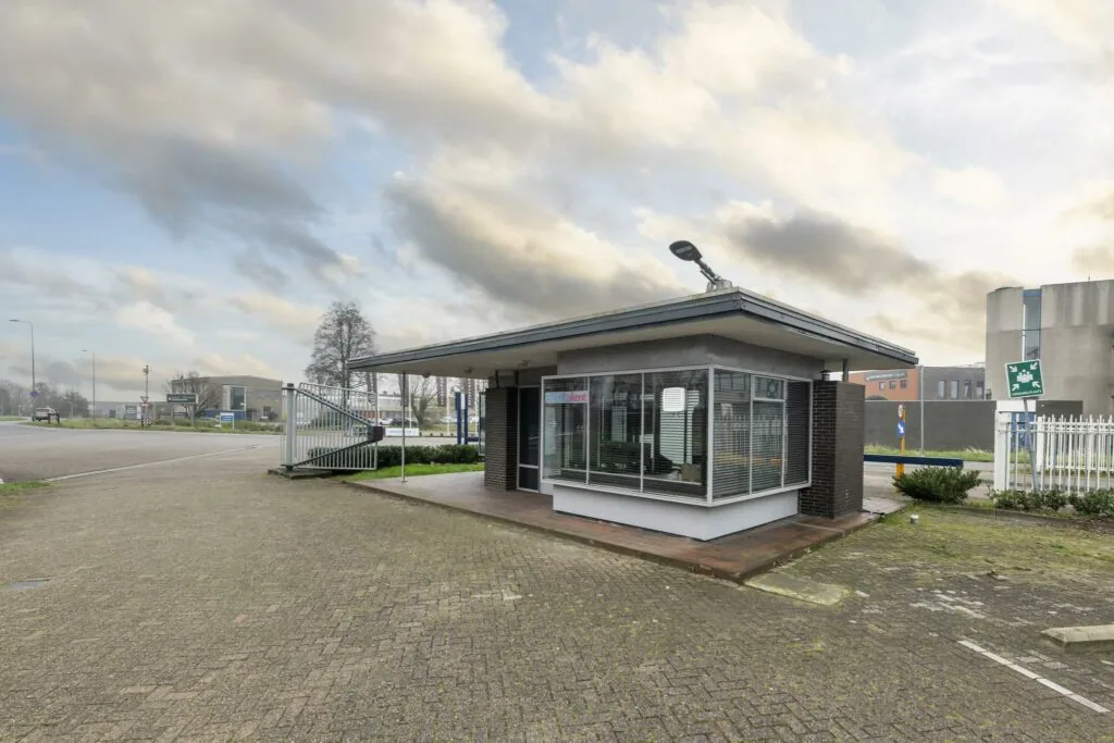 Wachtershuisje aan de Lindtsedijk met glazen gevel en slagboom bij industrieterrein.