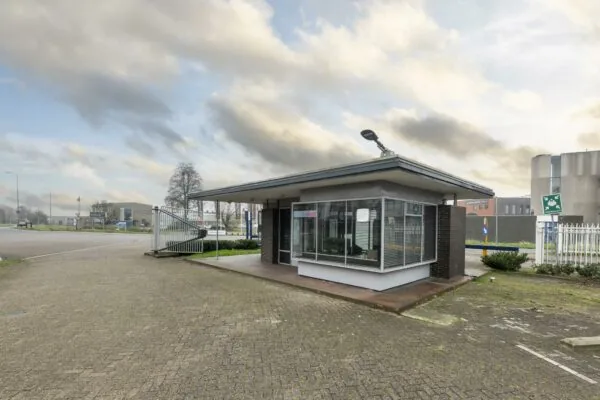 Wachtershuisje aan de Lindtsedijk met glazen gevel en slagboom bij industrieterrein.