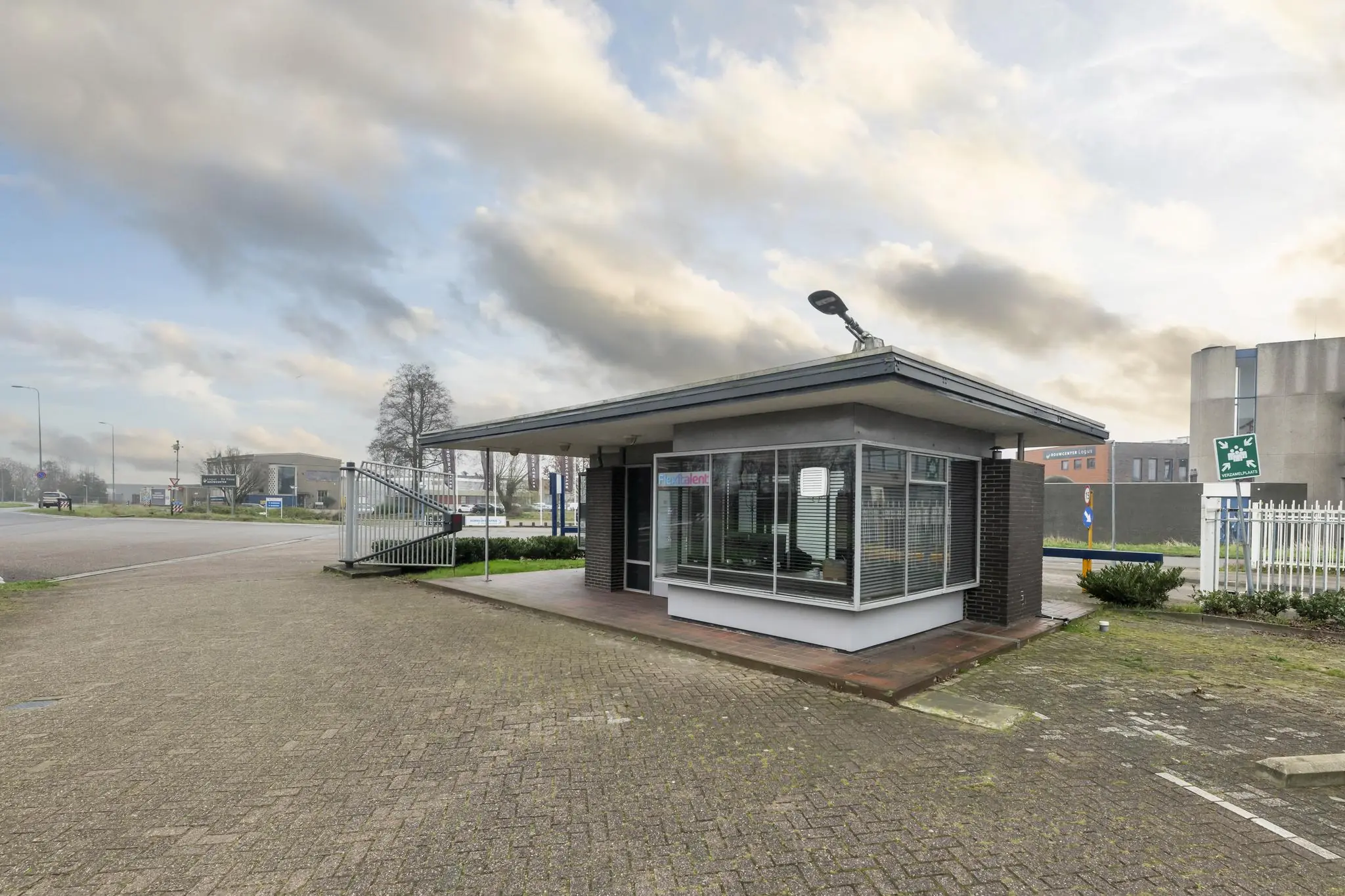 Wachtershuisje aan de Lindtsedijk met glazen gevel en slagboom bij industrieterrein.