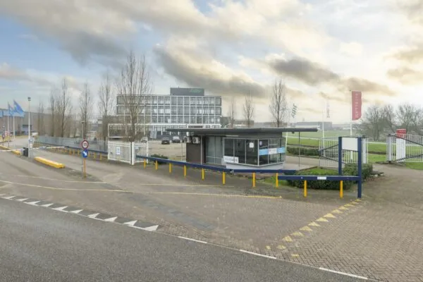 Ingang van een bedrijventerrein aan de Lindtsedijk met slagbomen, een portiersloge en het Jiffy-kantoorpand op de achtergrond.