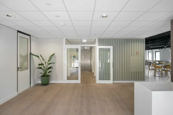 Moderne entreehal aan de Kralingseweg met houten vloer, glazen deuren en zicht op een lift en kantine.