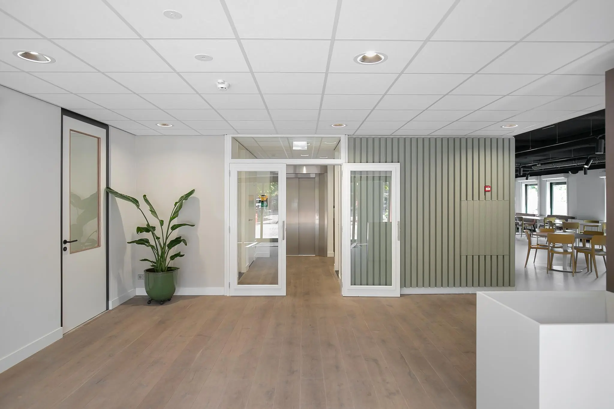 Moderne entreehal aan de Kralingseweg met houten vloer, glazen deuren en zicht op een lift en kantine.