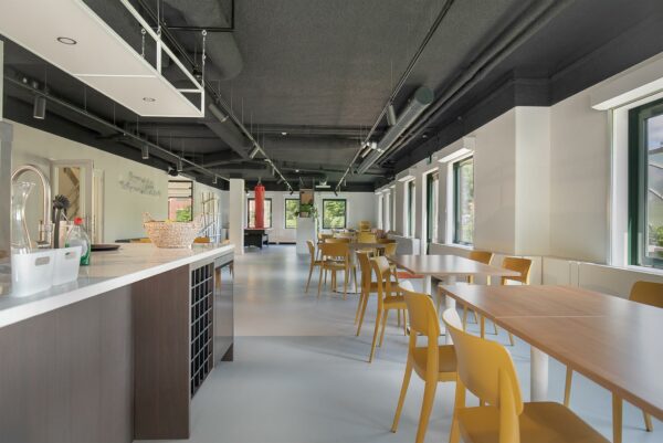 Moderne gemeenschappelijke ruimte aan de Kralingseweg met open keuken, gele stoelen en grote ramen.