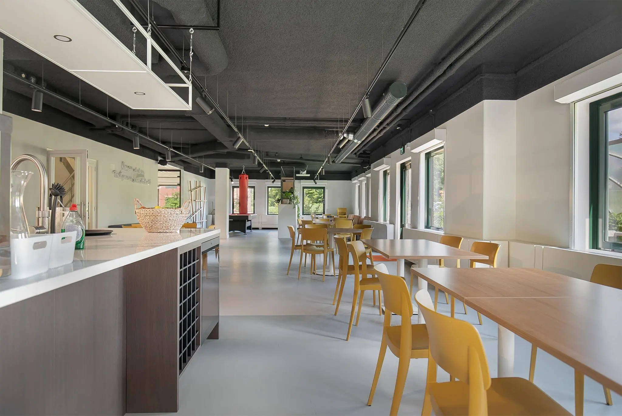 Moderne gemeenschappelijke ruimte aan de Kralingseweg met open keuken, gele stoelen en grote ramen.