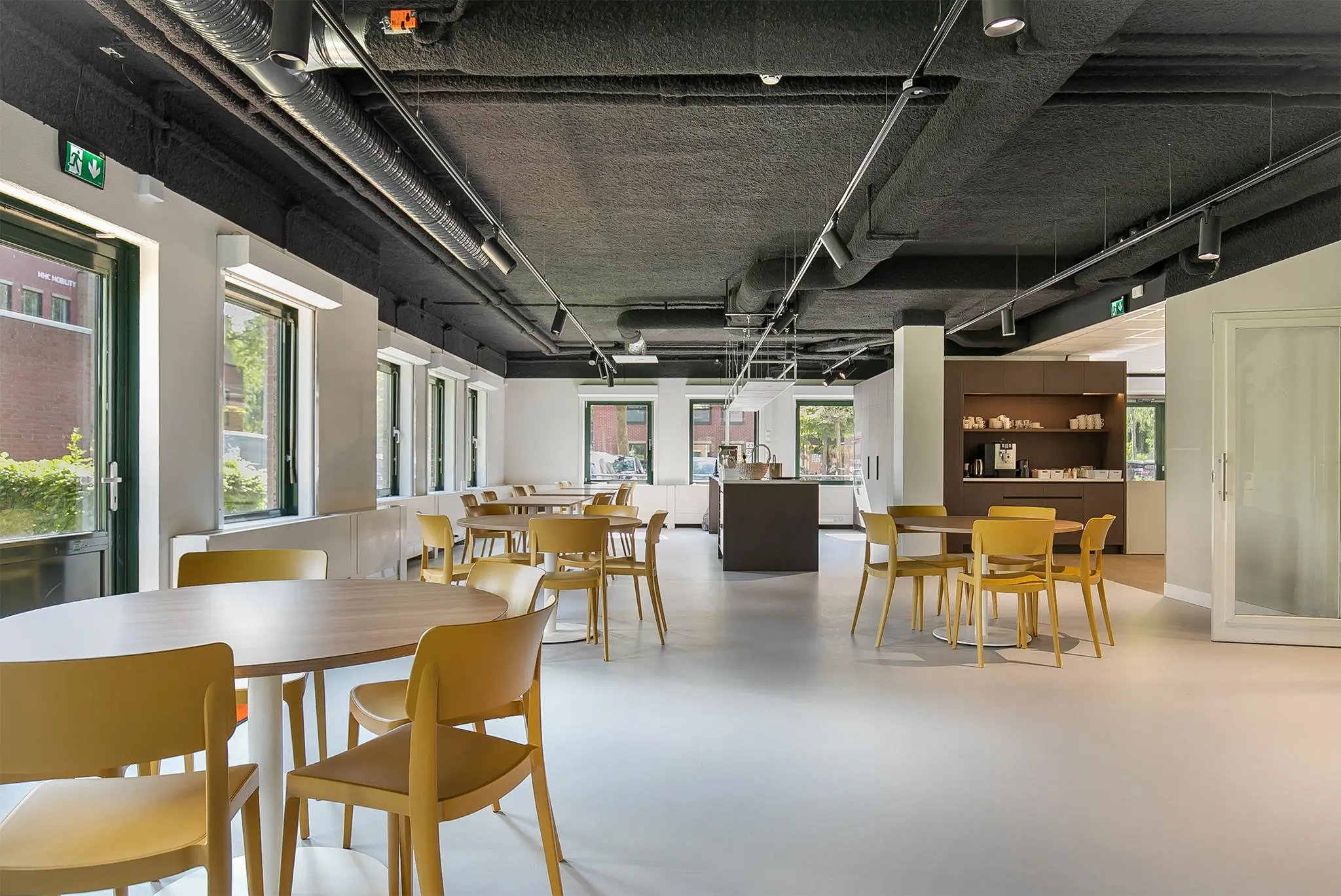 Moderne, open kantoorkantine aan de Kralingseweg met gele stoelen, ronde tafels en een koffiehoek.