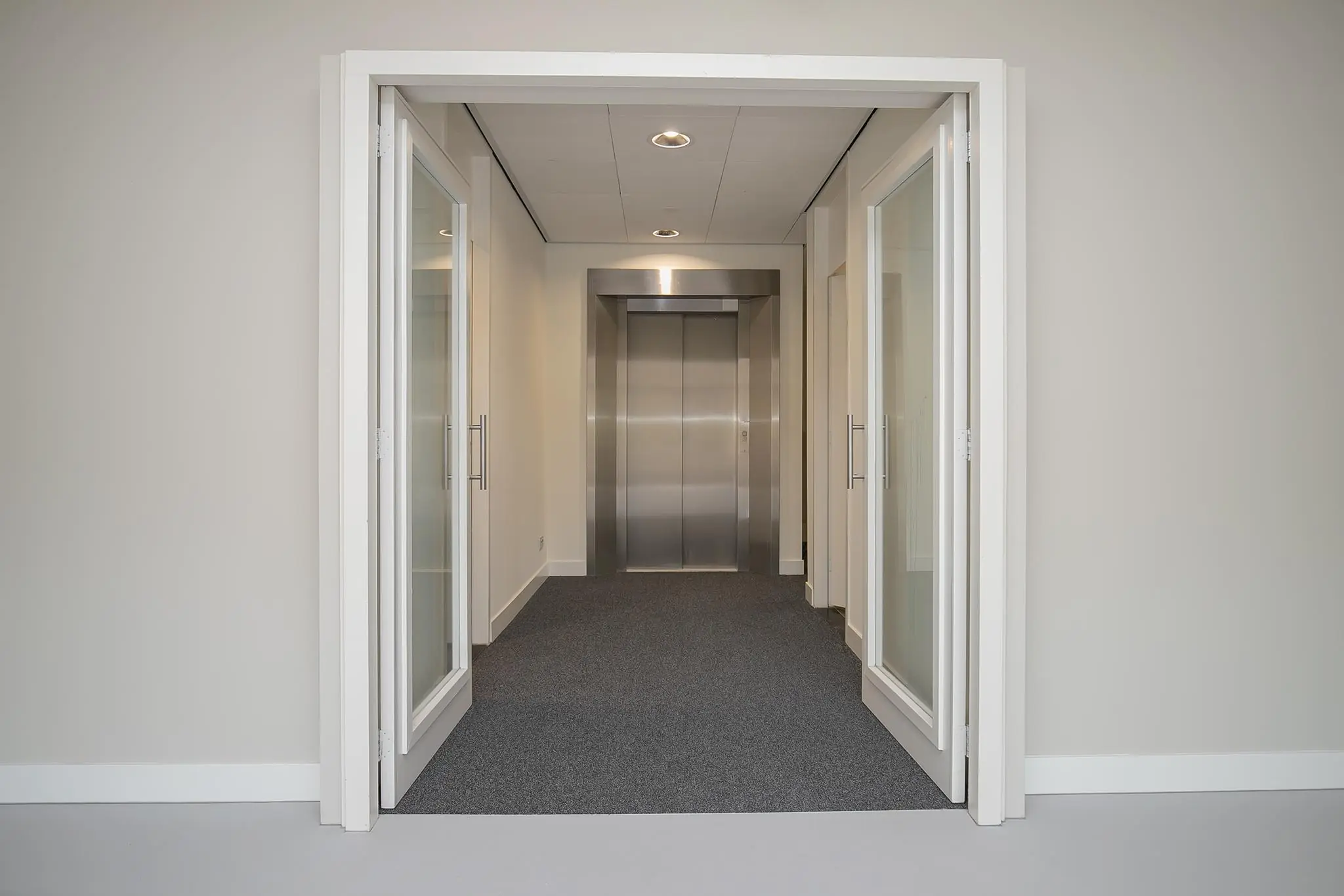 Hal met glazen deuren en een roestvrijstalen lift in een modern kantoorpand aan de Kralingseweg.