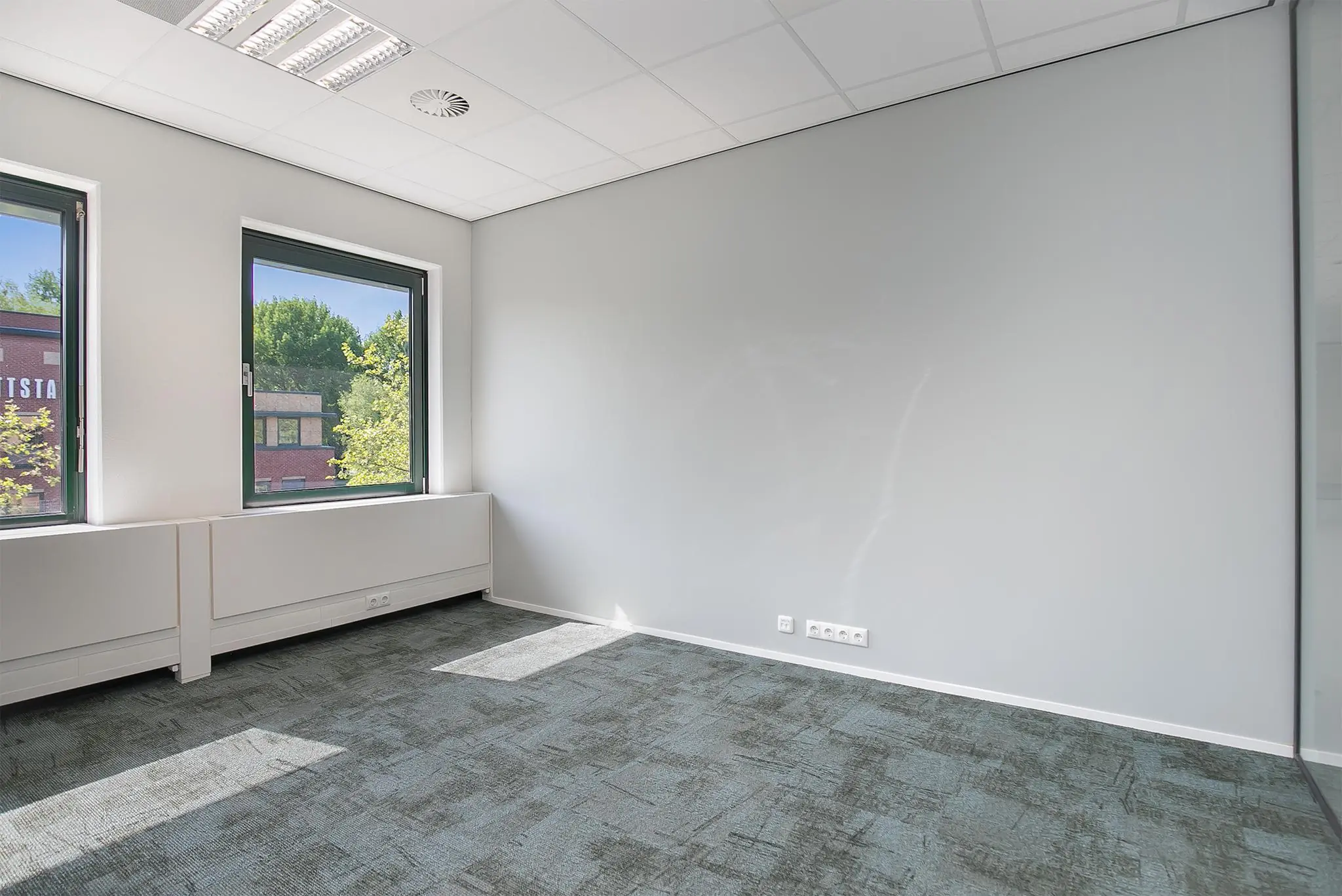 Licht en leeg kantoorruimte aan de Kralingseweg met twee ramen en grijs tapijt.