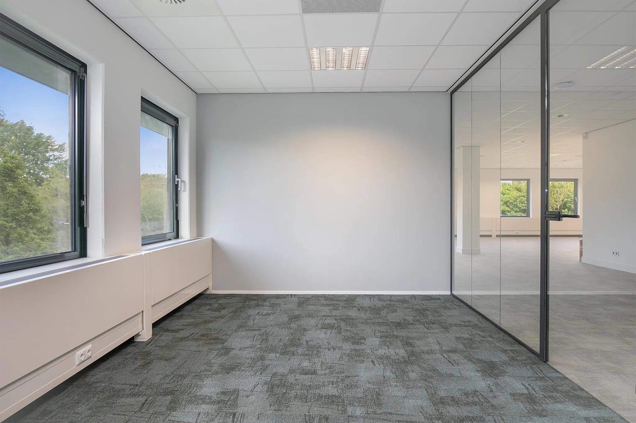 Licht en modern kantoorpand aan de Kralingseweg met grijs tapijt, grote ramen en glazen scheidingswand.