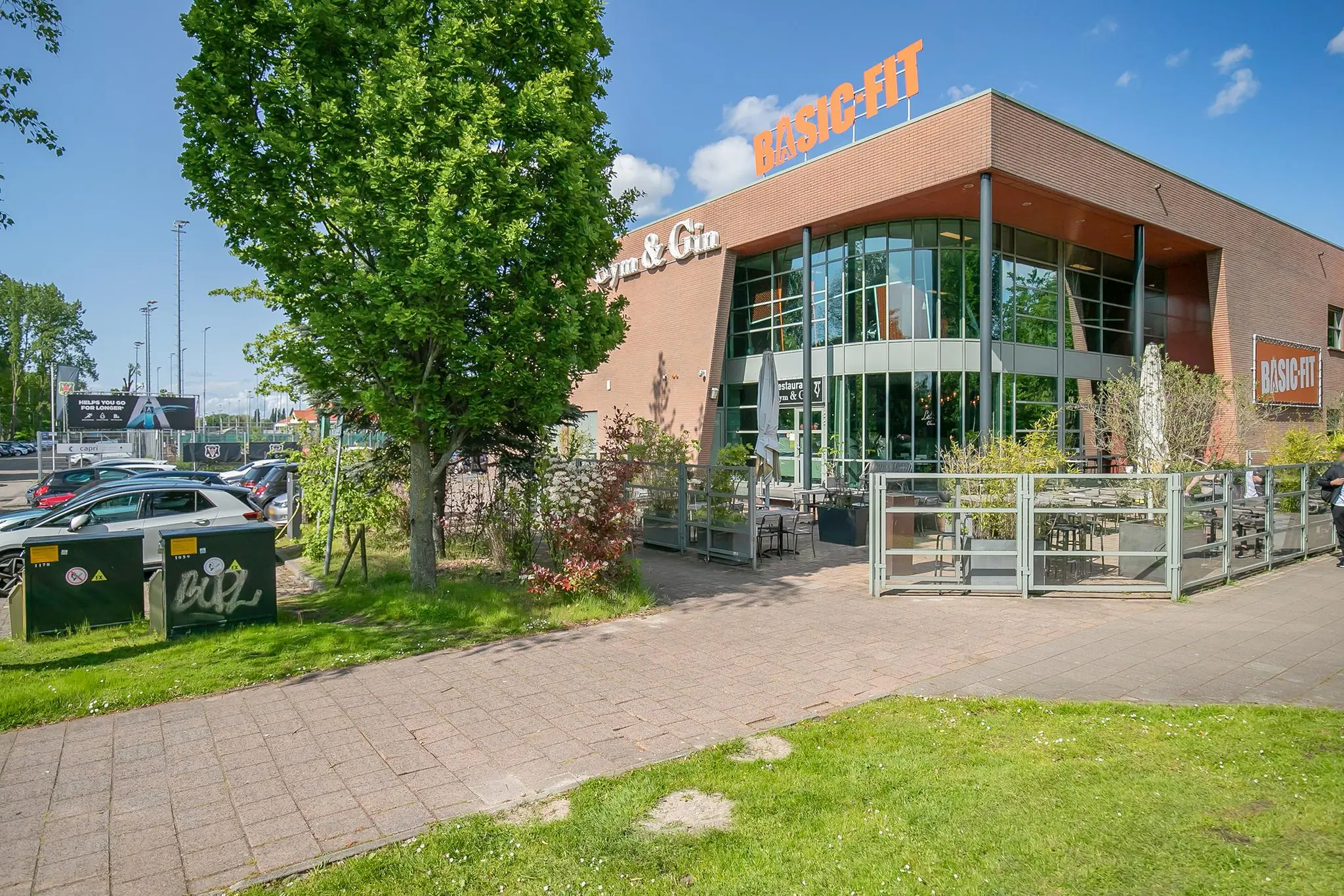 Vooraanzicht van het Basic-Fit gebouw aan de Kralingseweg met een terras en omliggend groen.