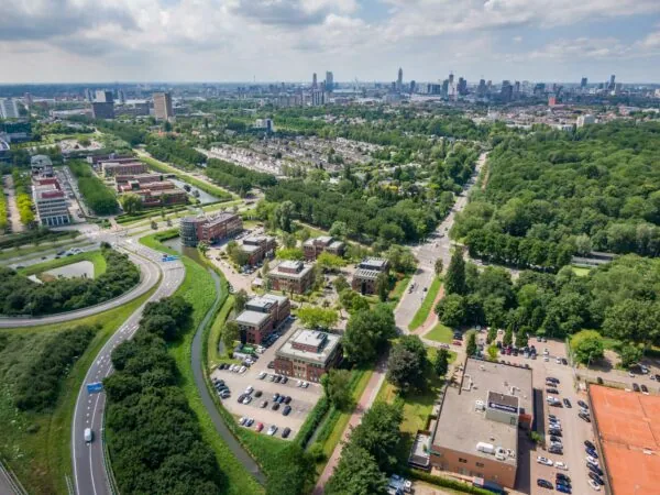 Luchtfoto van de Kralingseweg in Rotterdam met omliggende kantoren, woonwijken, groen en de skyline van de stad op de achtergrond.