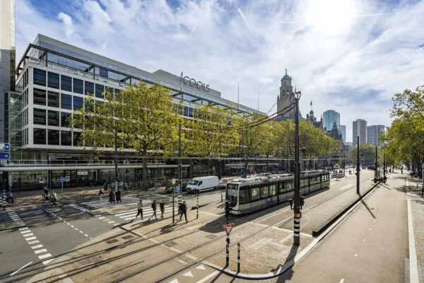 Straatbeeld van de Coolsingel in Rotterdam met een rijdende tram, voetgangers en moderne en historische gebouwen op de achtergrond.