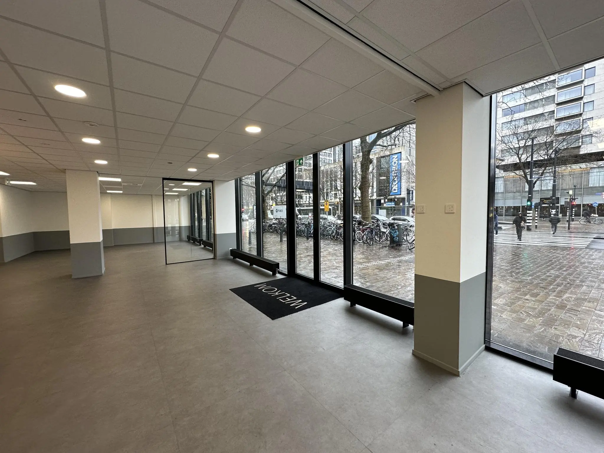 Leeg winkelpand met grote glazen ramen aan de Coolsingel in Rotterdam, uitkijkend op een drukke straat.