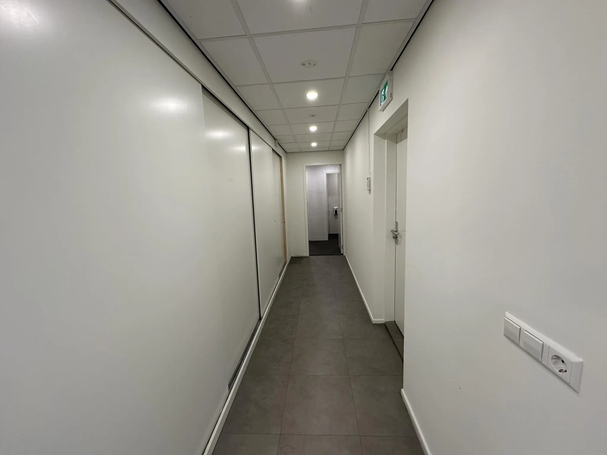 Witte, moderne gang in een kantoorgebouw aan de Coolsingel met grijze vloertegels en systeemplafond.