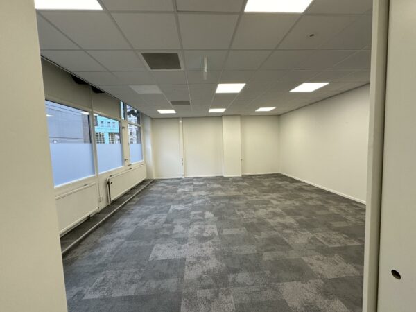 Leeg kantoorpand aan de Coolsingel met grijs tapijt, systeemplafond en grote ramen.
