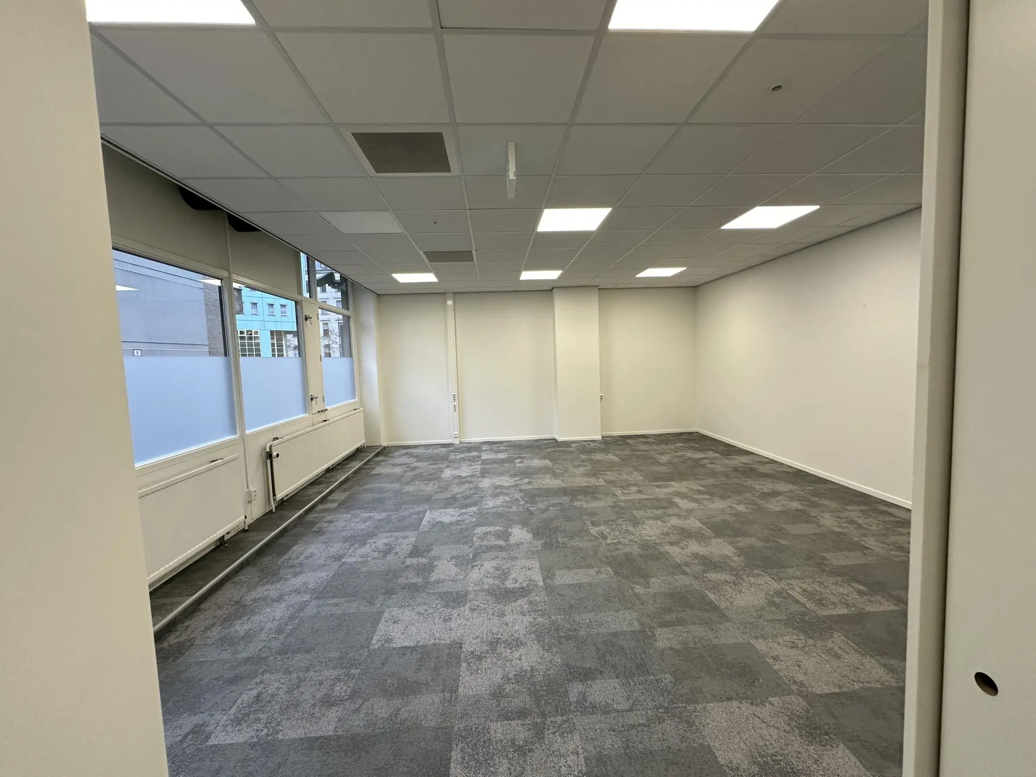 Leeg kantoorpand aan de Coolsingel met grijs tapijt, systeemplafond en grote ramen.