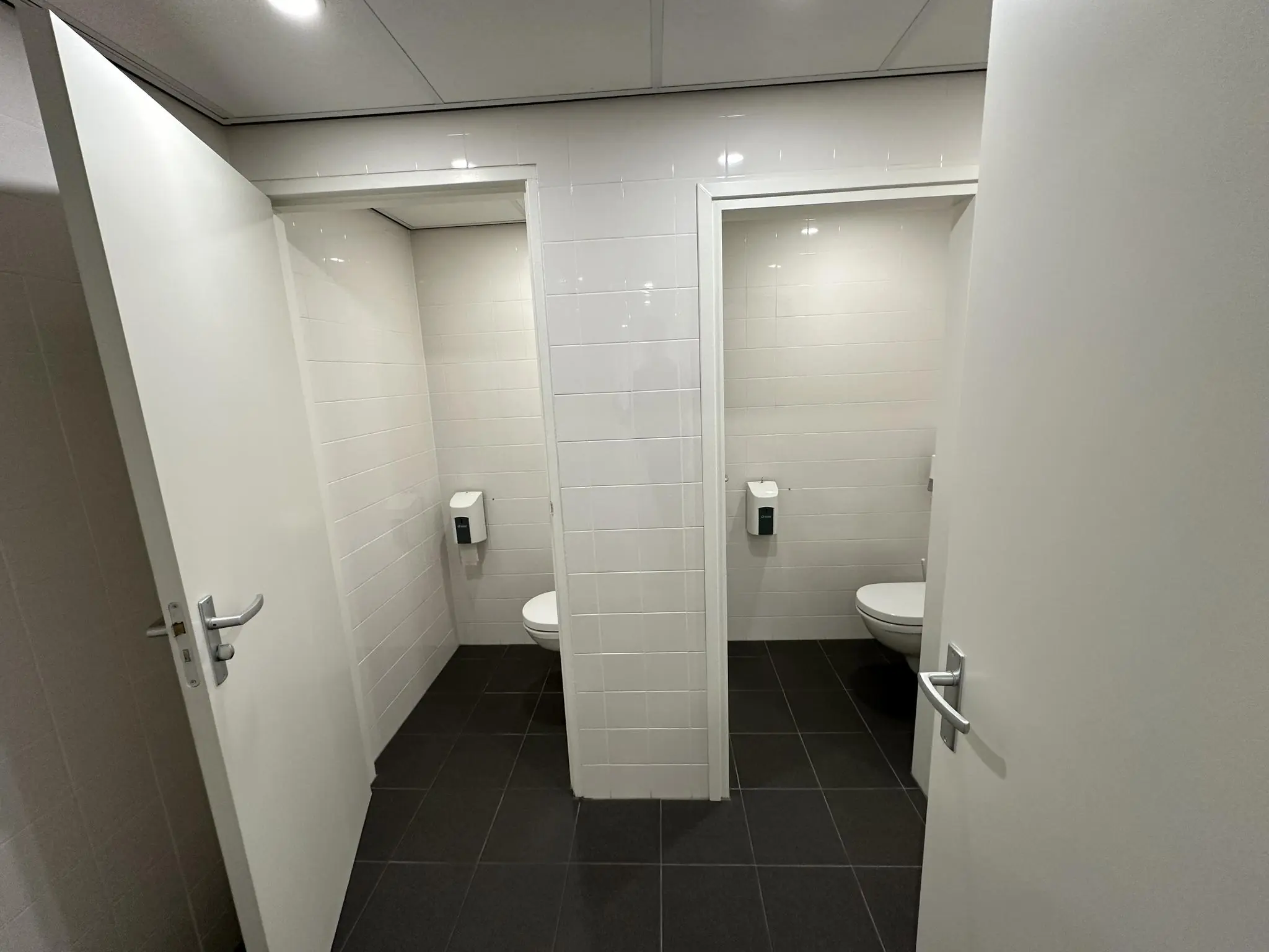 Twee deels geopende toiletdeuren in een openbare toiletruimte aan de Coolsingel met witte tegels en zwarte vloertegels.