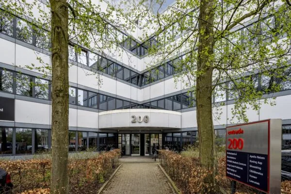 Ingang van het kantoorgebouw Entrada 200 met bedrijfsnamen op een informatiebord bij het pad.