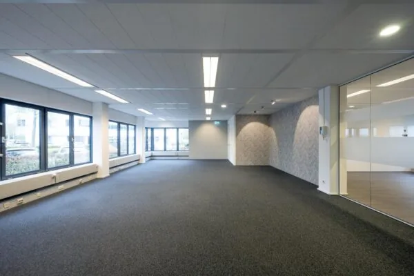 Licht en modern leeg kantoor met grote ramen, grijze vloerbedekking en een glazen wand.