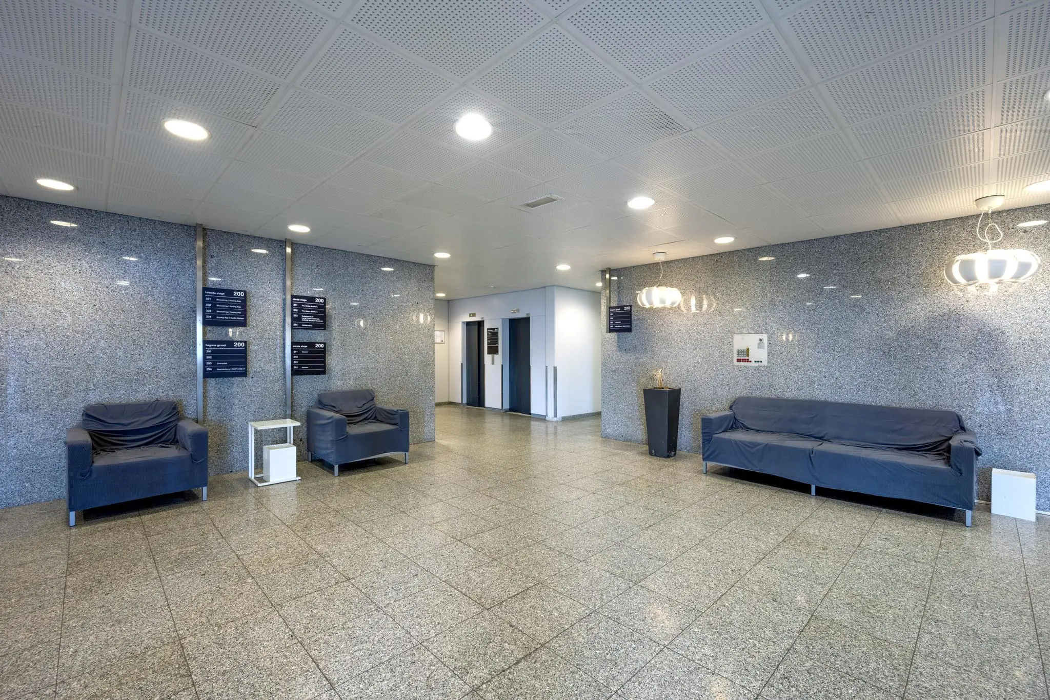 Moderne wachtruimte in een bedrijfsgebouw met grijze muren, zitbanken en liften.