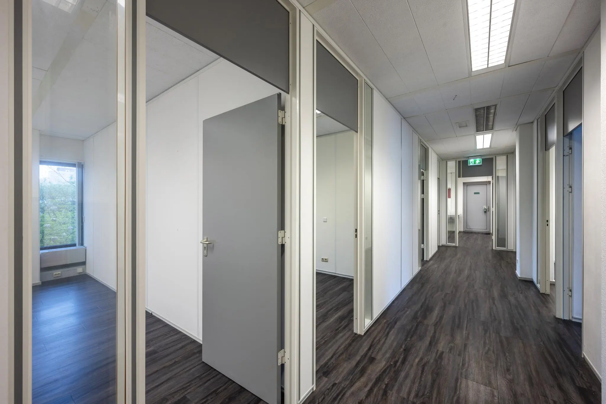 Een moderne kantoorhal met meerdere deuren en donker houtkleurig laminaat.