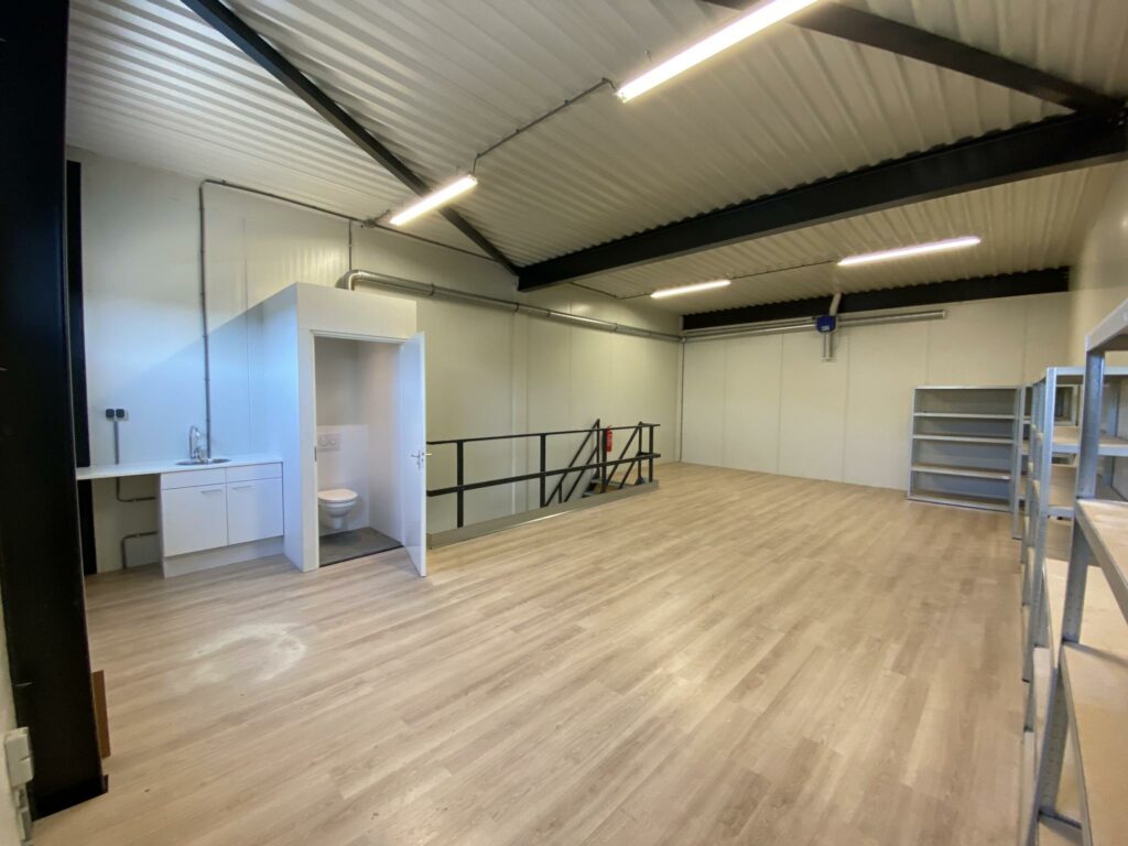 Ruimte op de Aalsmeerderweg met houten vloer, toilet, kitchenette en metalen wandstellingen.