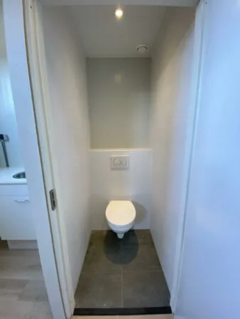 Kleine, smalle toiletruimte met een hangtoilet en grijze vloertegels aan de Aalsmeerderweg.