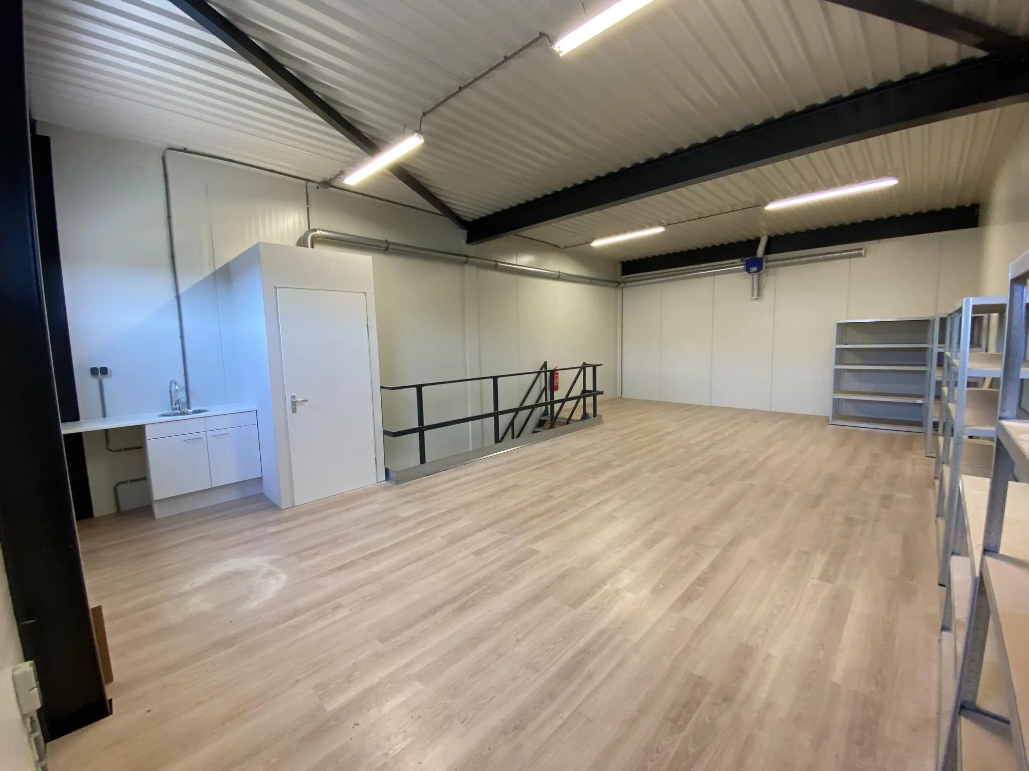 Ruimte met houten vloer, metalen stellingen, een keukenblok en een wit hok aan de Aalsmeerderweg.