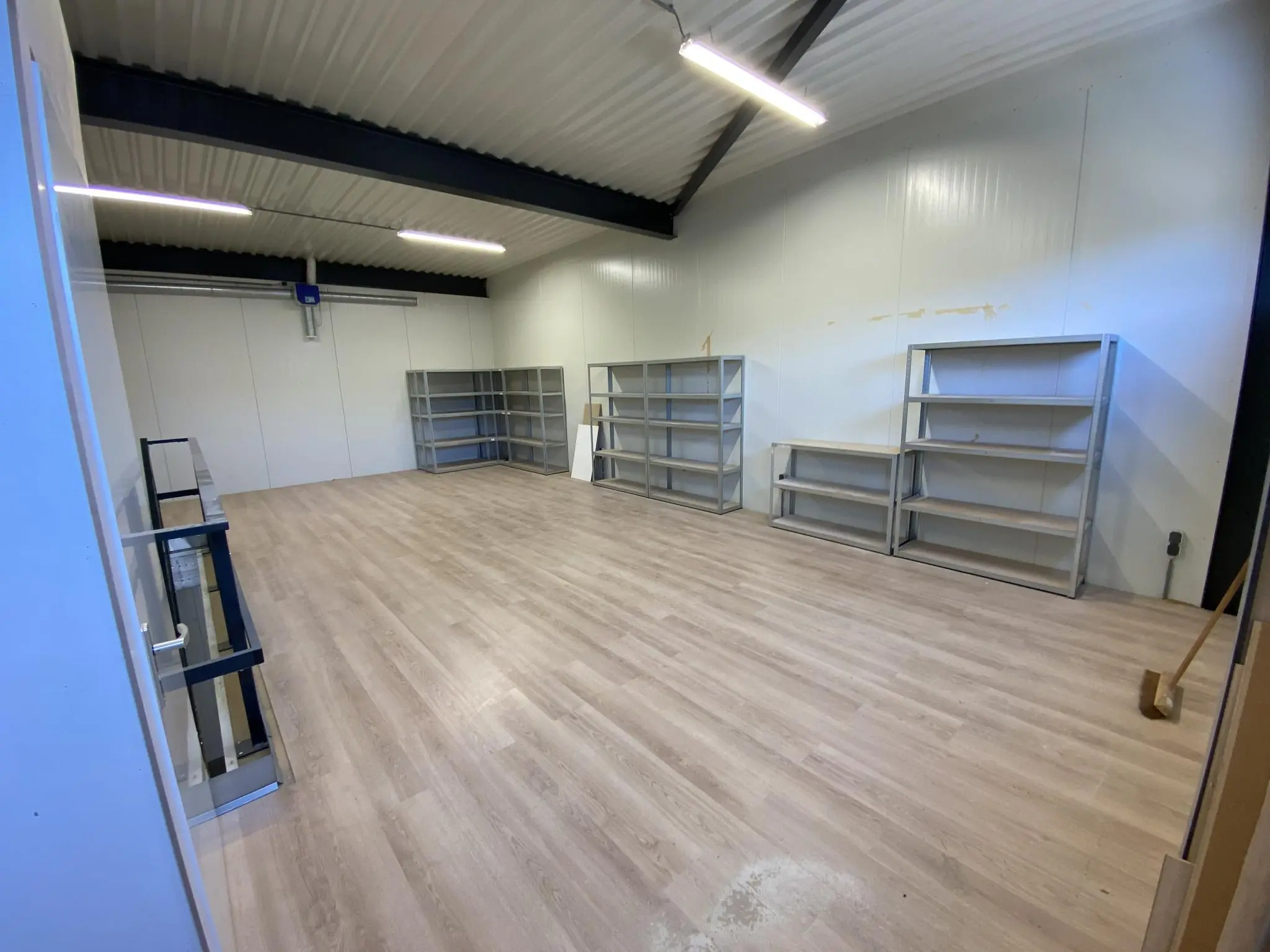Magazijnruimte aan de Aalsmeerderweg met houten vloer, metalen stellingen en wit afgewerkte wanden.