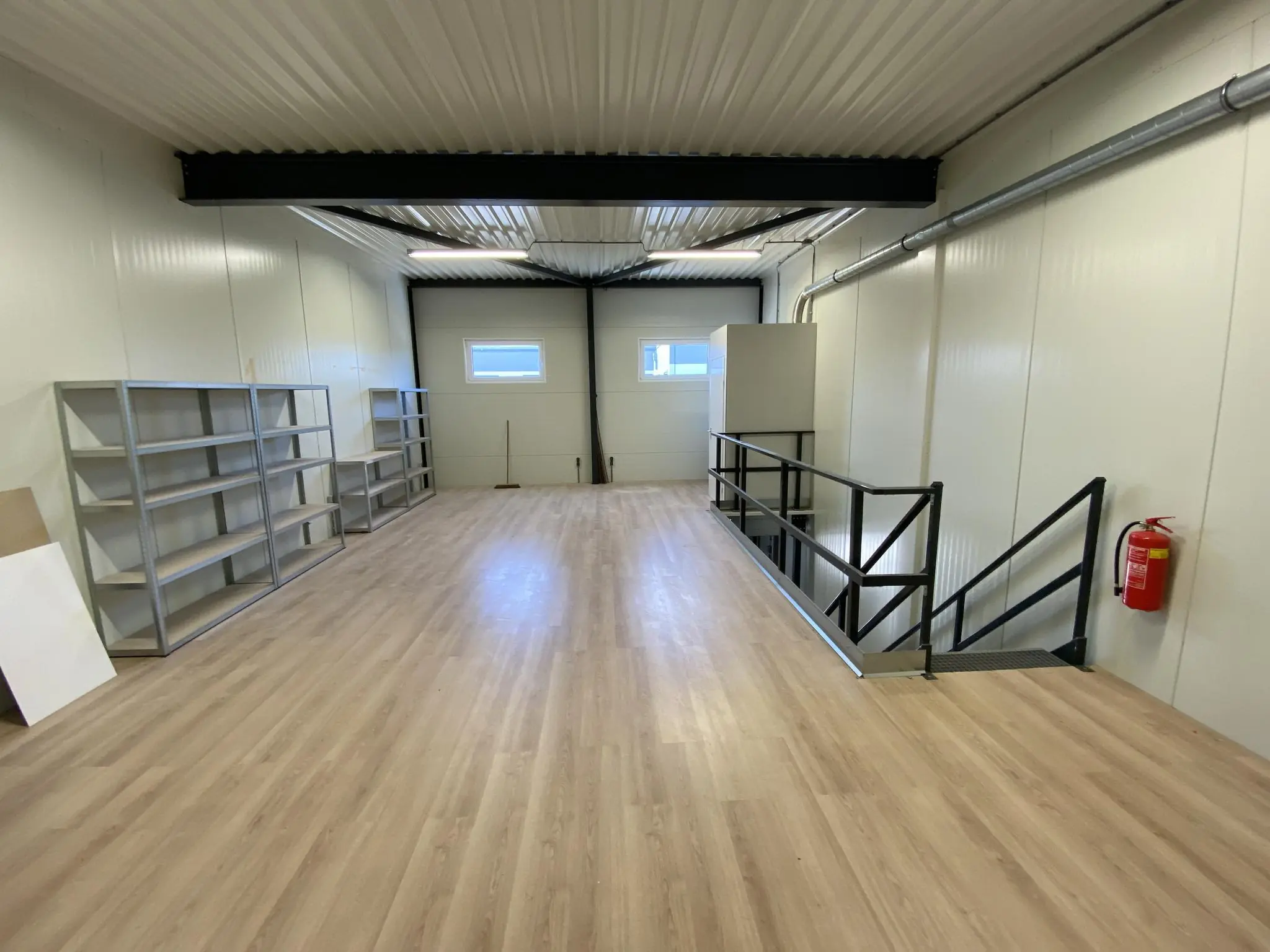 Opslagruimte met houten vloer, metalen stellingen, trap met zwart hekwerk en brandblusser aan de muur aan de Aalsmeerderweg.