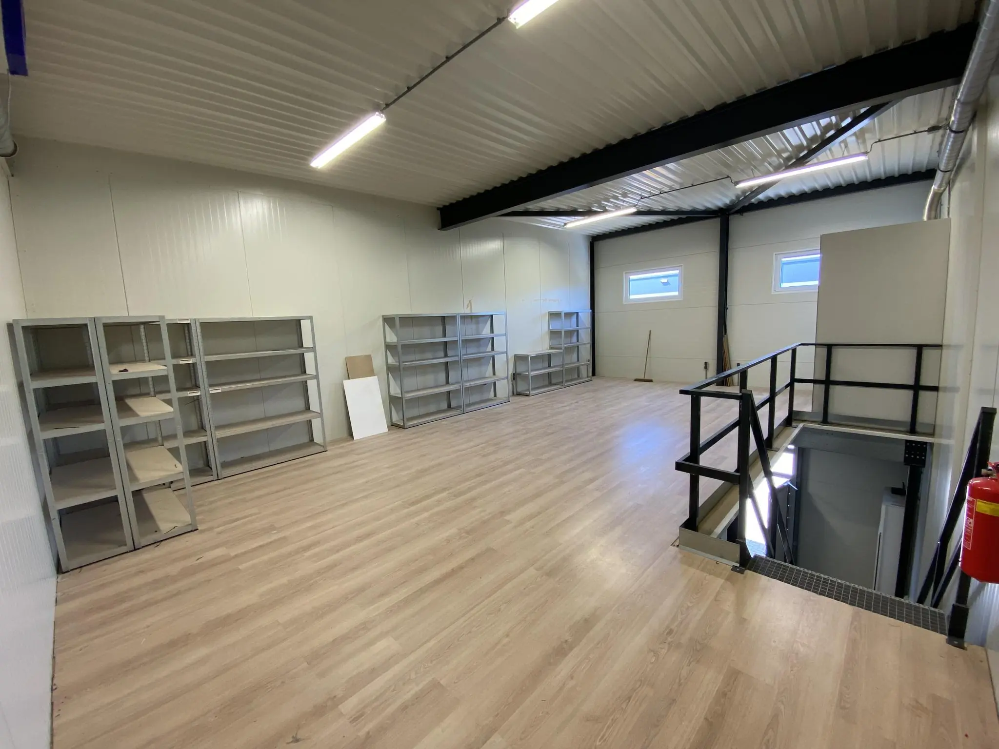 Ruimte op de bovenverdieping van een bedrijfspand aan de Aalsmeerderweg met houten vloer, metalen stellingen en een trap met zwart hekwerk.