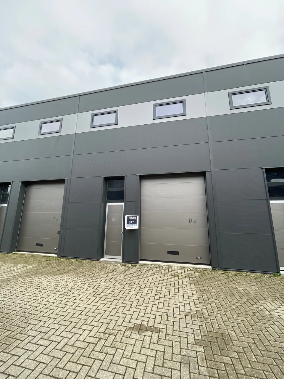 Grijs bedrijfsunit aan de Aalsmeerderweg met te huur-bord bij deur D.07.