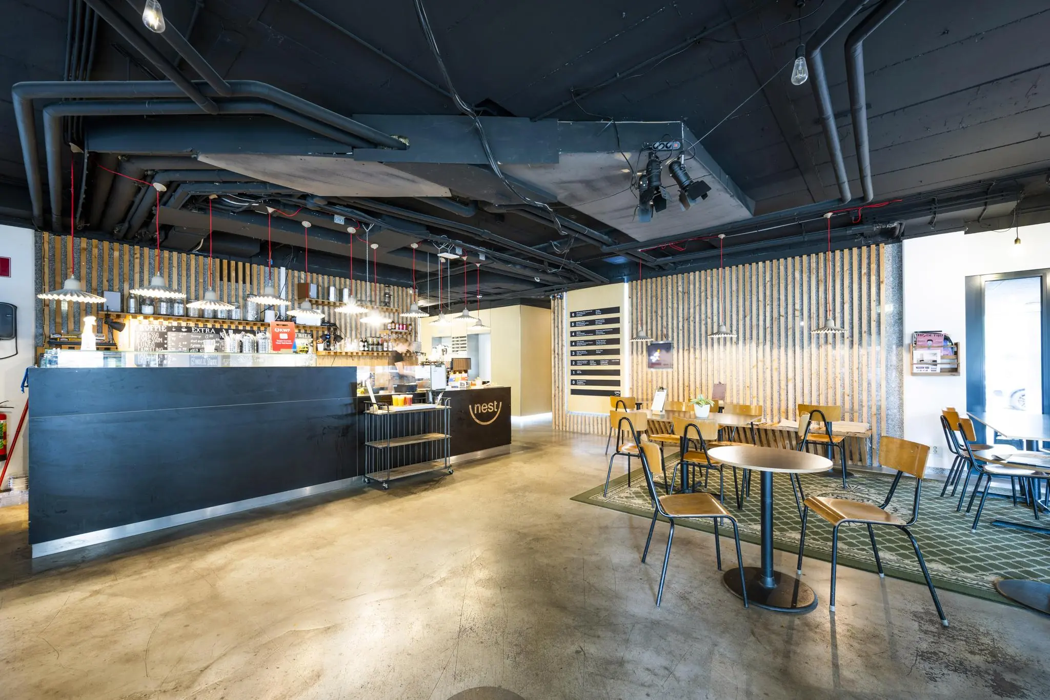 Modern ingerichte koffiebar "Nest" met houten tafels, industriële details en een gezellige zithoek.