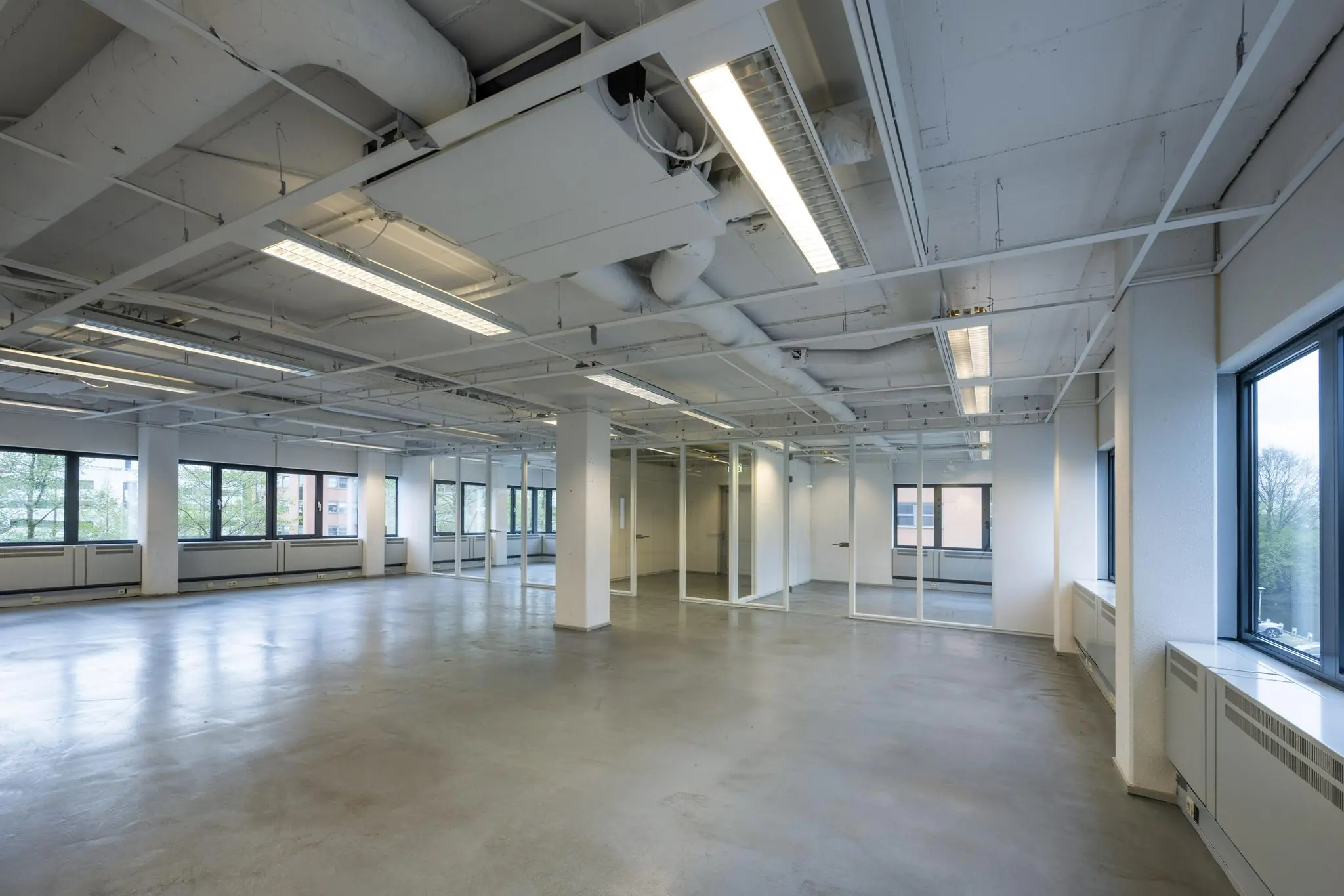 Lege, moderne kantoorruimte met glazen wanden, grote ramen en zicht op het systeemplafond.