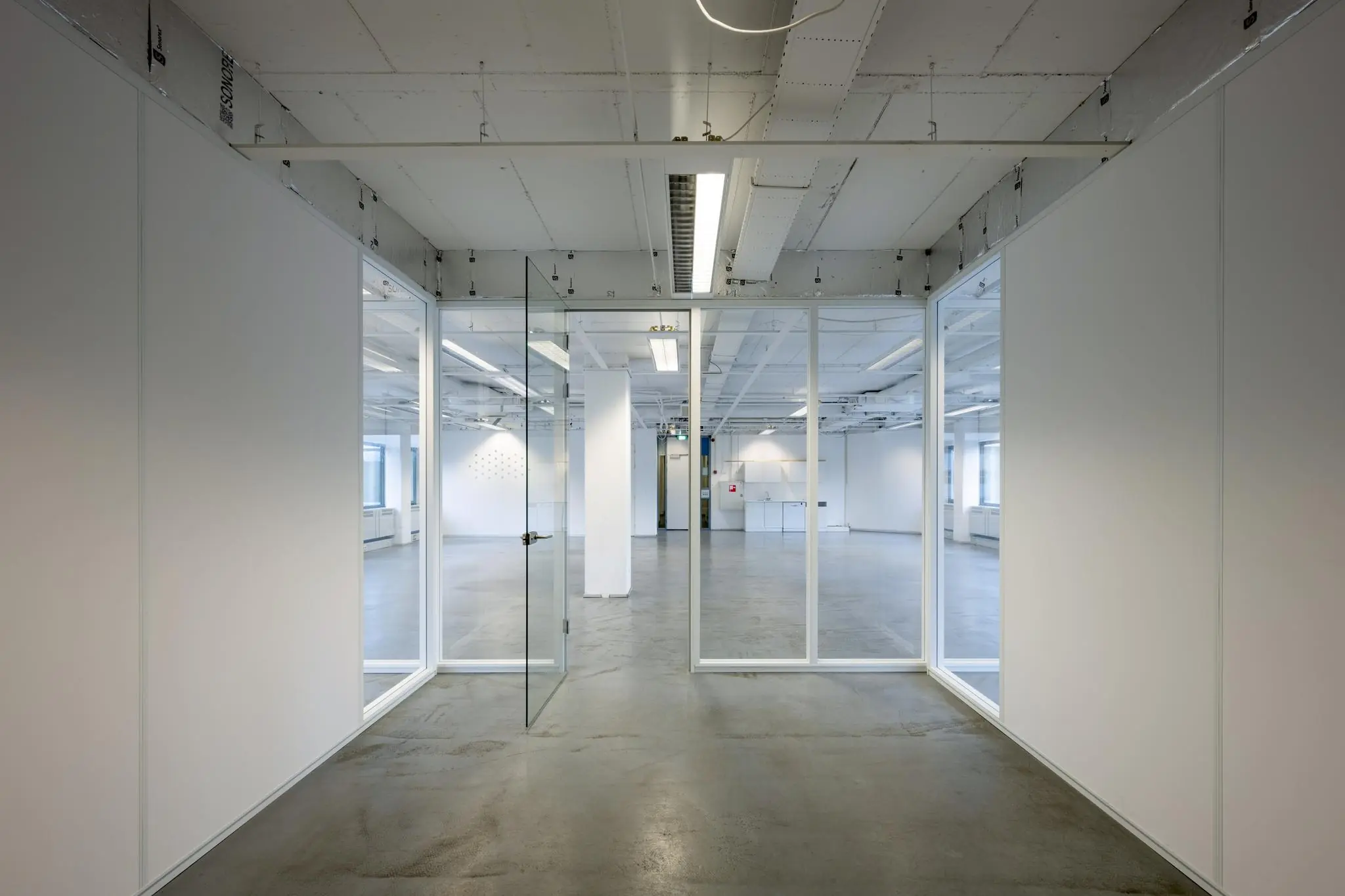 Lege, moderne kantoorruimte met glazen wanden en betonnen vloer.