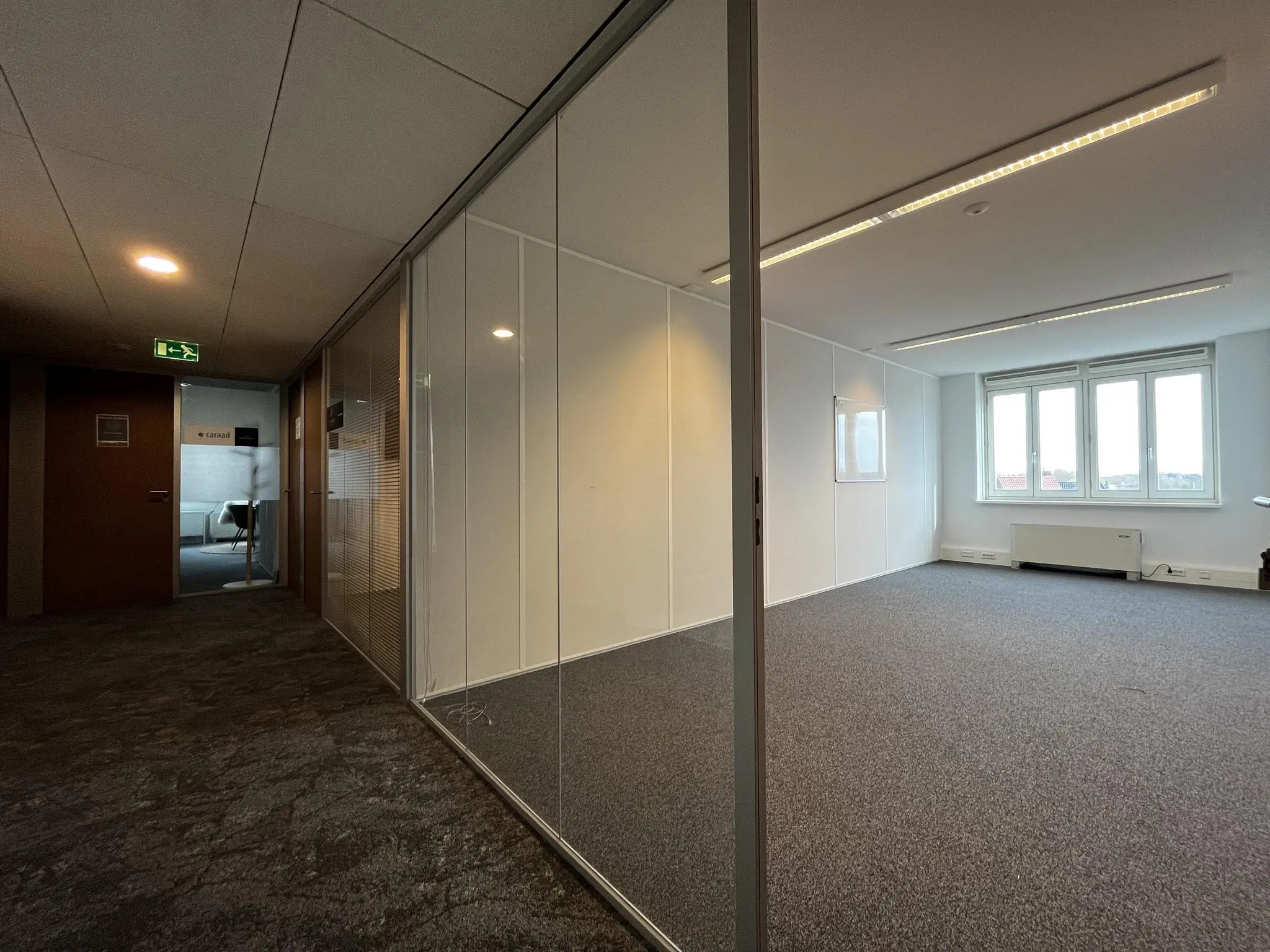 Leeg kantoor met glazen wanden in gebouw Middenburcht, met uitzicht op een gang en een vergaderruimte.