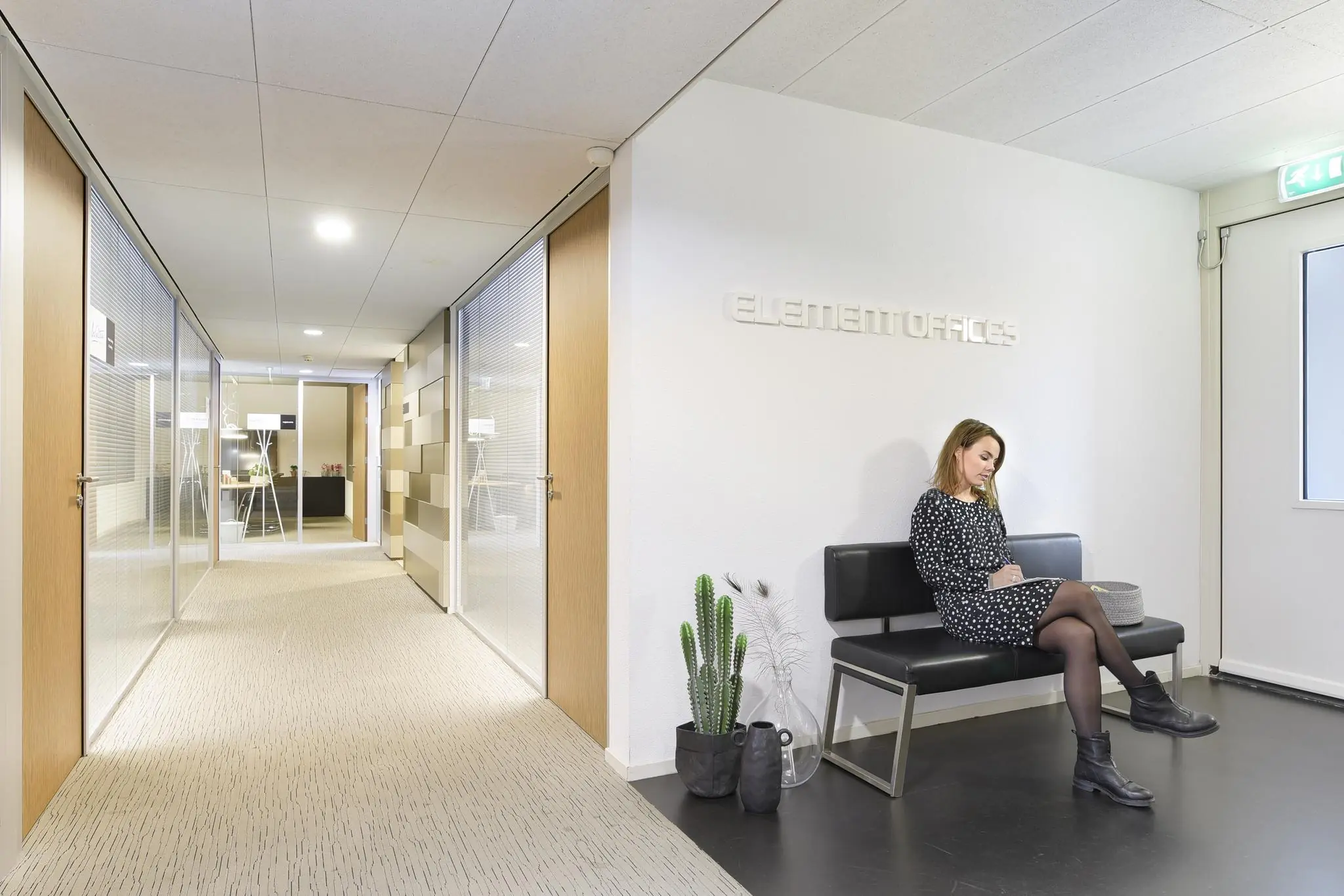 Vrouw zit in de wachtruimte van Element Offices Middenburcht op een zwarte bank in een moderne kantooromgeving.