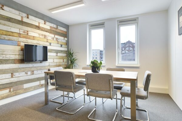 Vergaderruimte met houten accenten, zes stoelen, een plant op tafel en uitzicht op het gebouw Middenburcht.