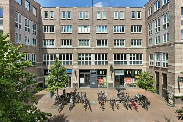 Binnenplein van kantoorgebouw Middenburcht met fietsenrekken, winkels en kantoren aan een gevel van baksteen.