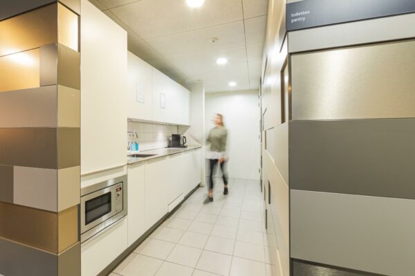 Moderne, lichte pantry in kantoorgebouw Middenburcht met witte kasten en een persoon in beweging.