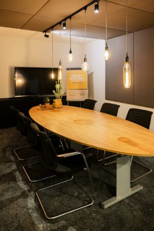 Vergaderruimte Middenburcht met ovale houten tafel, moderne stoelen, hanglampen en presentatiescherm.