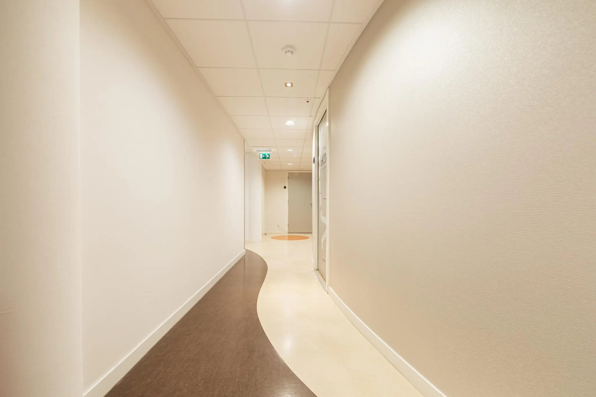 Lichte, modern ontworpen gang in zorginstelling Middenburcht met golvend patroon in de vloer.