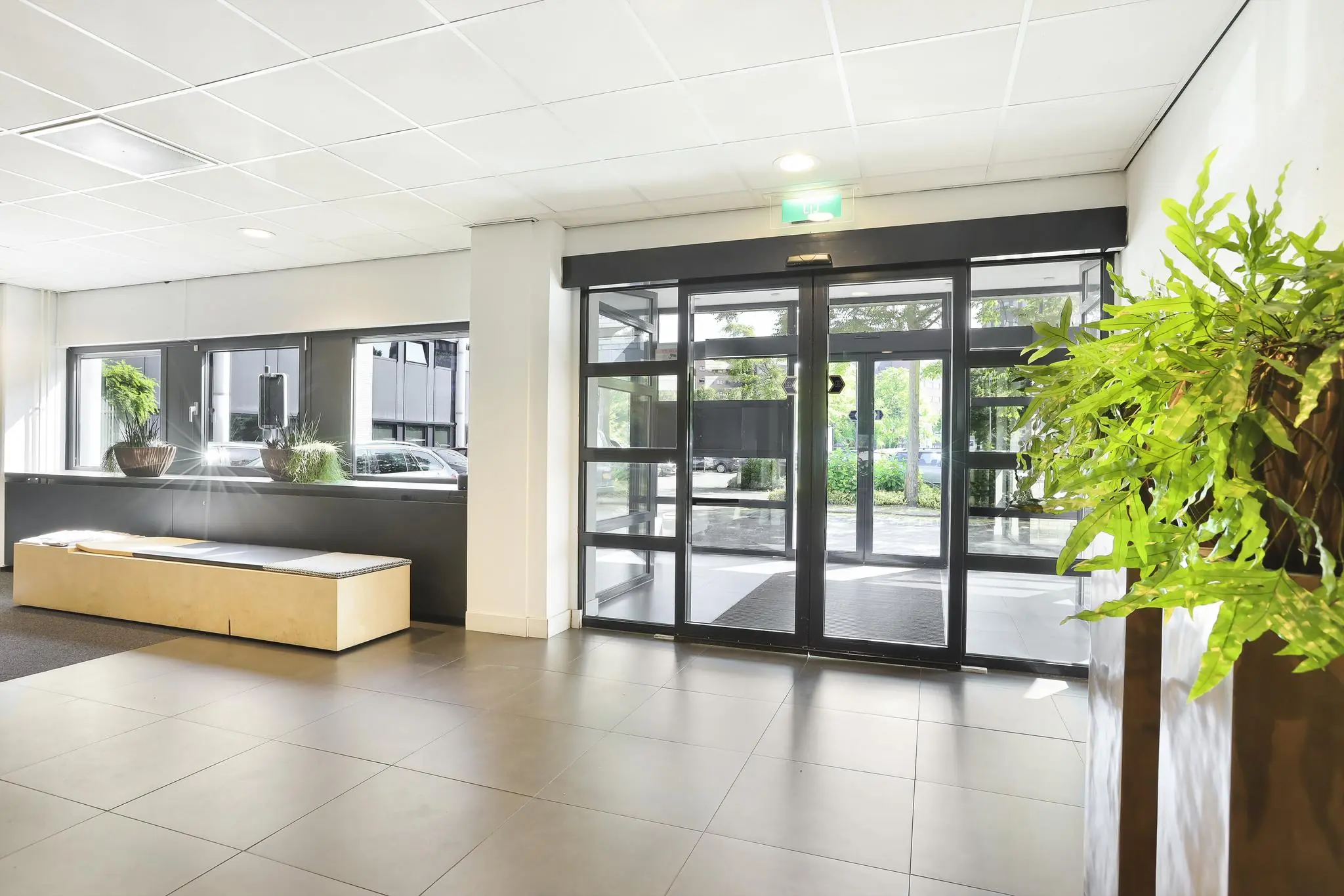 Moderne en lichte entreehal aan de Winthontlaan met glazen draaideur, zitbank en kamerplanten.