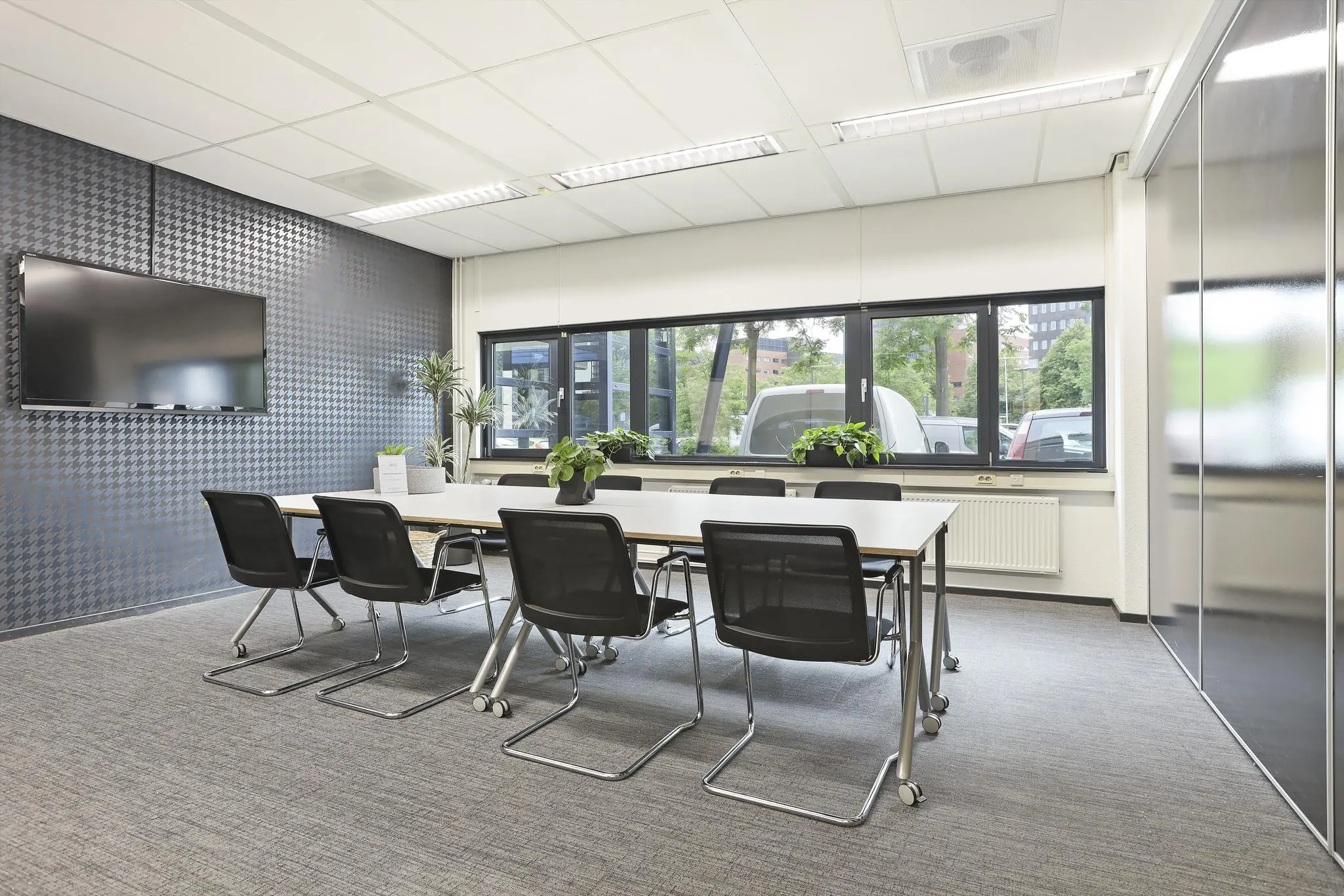 Moderne vergaderruimte aan de Winthontlaan met een grote tafel, zwarte stoelen, planten en een flatscreen aan de muur.