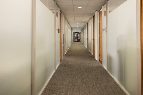 Lange, rechte kantoorgang aan de Winthontlaan met glazen wanden en gesloten deuren.