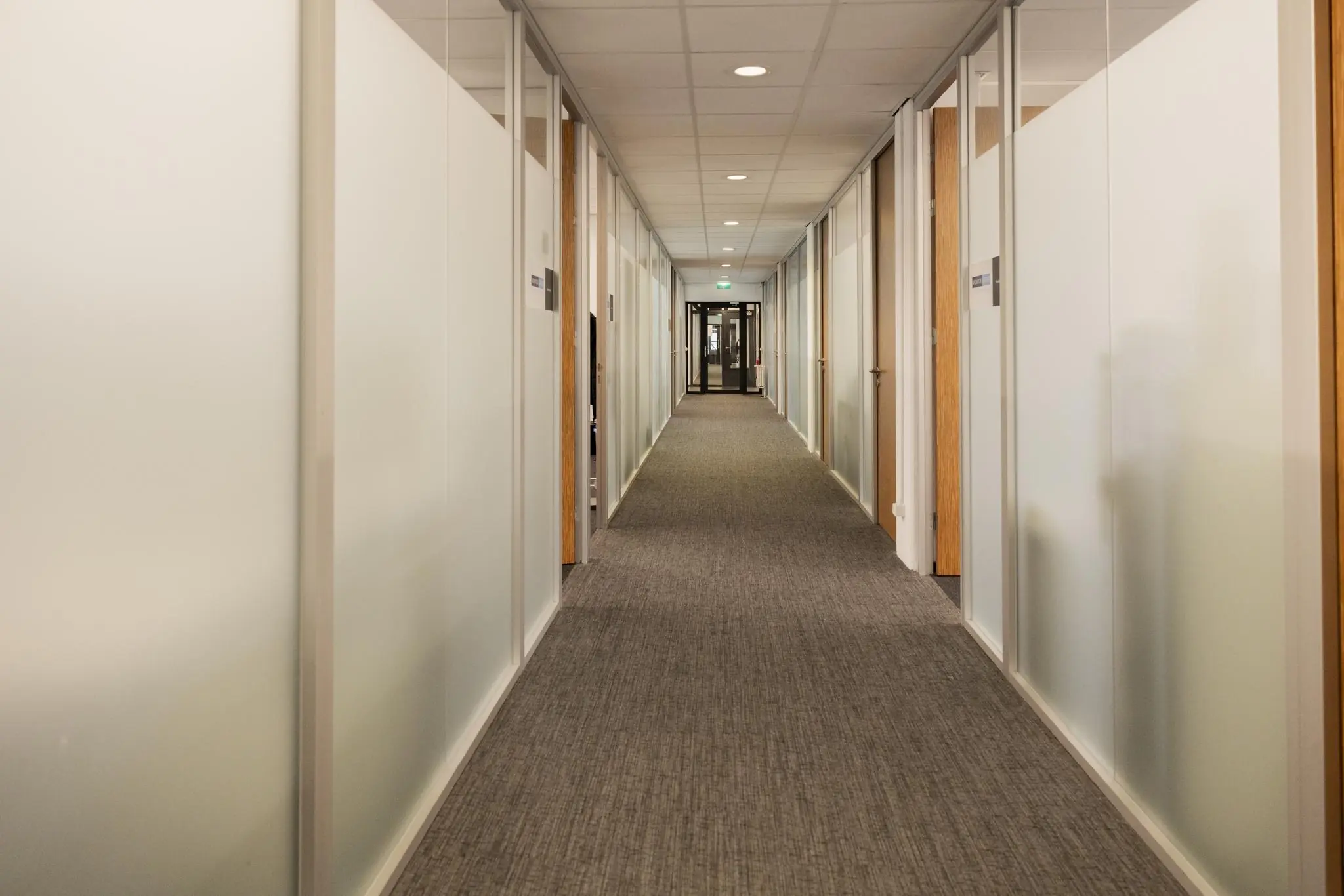 Lange, rechte kantoorgang aan de Winthontlaan met glazen wanden en gesloten deuren.