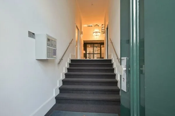 Entree met trap en glazen deur in een gerenoveerd pand aan de Koninginnegracht, verlicht door een kroonluchter.