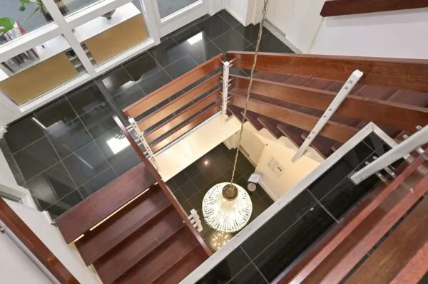 Houten trap met moderne leuningen in een pand aan de Koninginnegracht, met uitzicht op een kroonluchter en glanzende zwarte vloertegels.