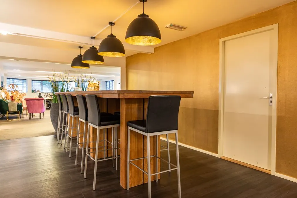 Moderne vergaderruimte aan de Koninginnegracht met hoge houten tafel, zwarte barkrukken en hanglampen.