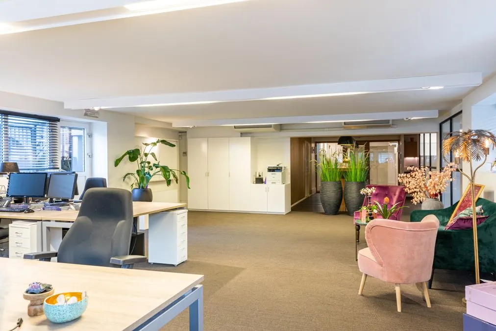 Modern kantoorinterieur aan de Koninginnegracht met bureaus, kleurrijke fauteuils en grote planten.