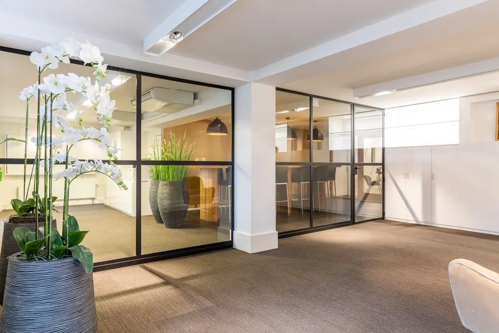 Modern kantoorpand aan de Koninginnegracht met glazen wanden, grote planten en een strakke inrichting.
